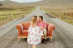 two women sitting on an orange chair in the middle of a dirt road, facing each other