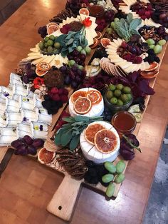 an assortment of fruits and cheeses laid out on a long wooden table with other food items