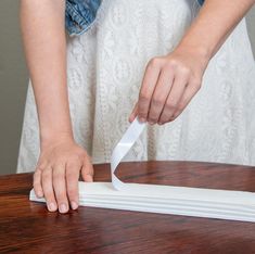 a woman is cutting paper on top of a piece of wood with a white handle