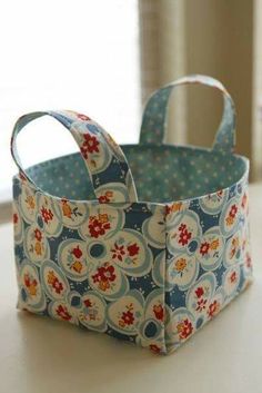 a small blue and red flowered fabric basket on a white table with a mirror in the background