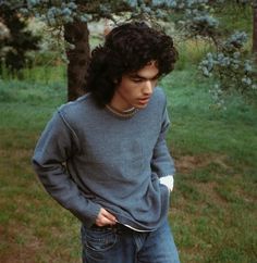 a young man standing in the grass with his hands on his hips and looking down