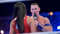 a man holding a microphone talking to a woman in a wrestling ring with lights behind him