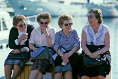 three women sitting on a bench next to each other in front of water and boats