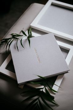 two white frames sitting next to each other on top of a table with green plants