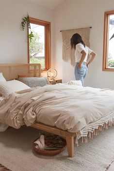 a woman standing on the edge of a bed in a room with two large windows