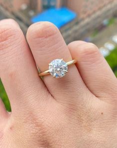 a person's hand with a diamond ring on top of their finger, in front of a building