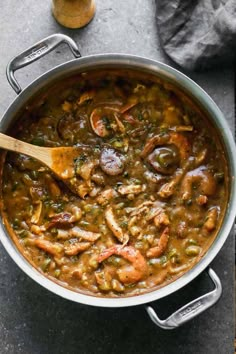 a pot filled with shrimp and green beans on top of a table next to a wooden spoon