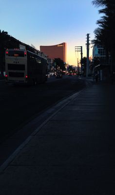 a city street at dusk with the sun setting in the background and palm trees on both sides