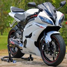 a white and black motorcycle parked on top of a dirt road in front of trees