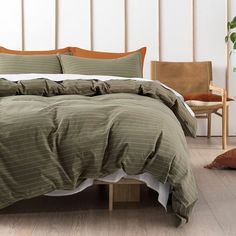 a bed with green and white comforter in a room next to a chair, potted plant and wooden floor