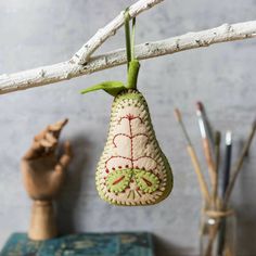 an ornament hanging from a twig on a branch with paintbrushes in the background