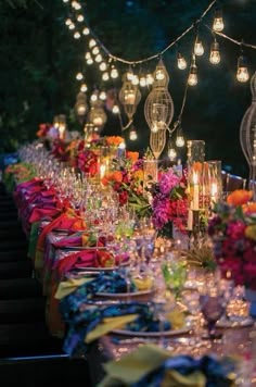 a long table covered in lots of glasses and plates with lit candles on top of them