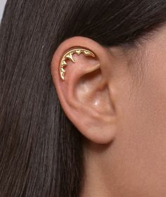 a close up of a person wearing a gold ear cuff with two bats on it