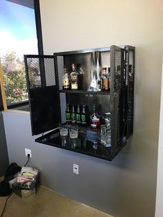 a wall mounted shelf with liquor bottles and glasses on it in front of a window