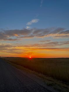 the sun is setting over an empty road in the middle of nowhere, with tall grass on both sides