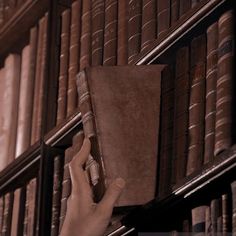 a hand holding a book in front of a bookshelf full of old books