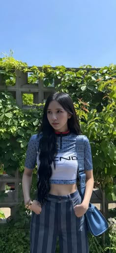 a woman with long black hair standing in front of a fence and wearing striped pants