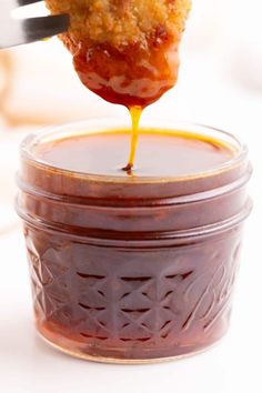 a spoon is lifting some food out of a jar filled with honey and sauces