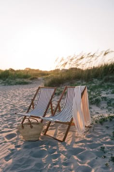 two lawn chairs sitting on top of a sandy beach