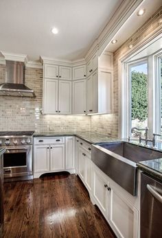 a kitchen with white cabinets and wood floors, stainless steel sink and dishwasher