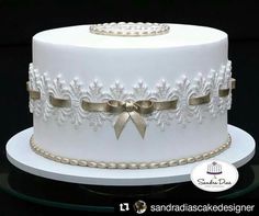 a white wedding cake with gold ribbon and bow on the top is sitting on a glass platter