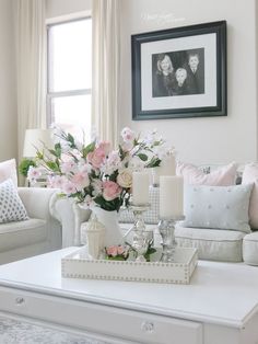 a living room with white furniture and pink flowers on the coffee table in front of a window