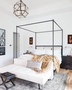 a white bedroom with four poster bed and pictures on the wall above it's headboard