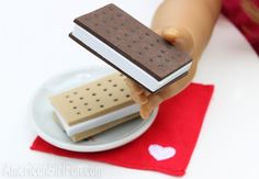 a doll's hand holding an ice cream sandwich on top of a white plate