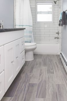 a white bathroom with wood flooring and gray tile on the shower wall, toilet and bathtub