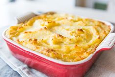 a red casserole dish with cheese in it on a white cloth and napkin