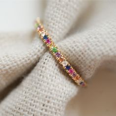 a gold colored ring with multicolored stones on it's side sitting on top of a white cloth