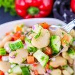 a white bowl filled with bean salad next to red peppers and broccoli in the background