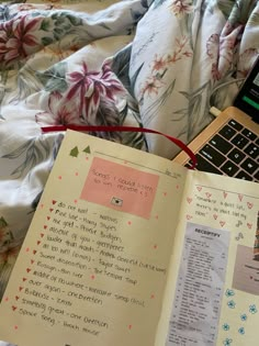 an open book sitting on top of a bed next to a cell phone and laptop computer