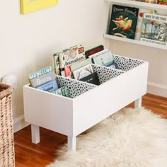 a white table with books and magazines in it next to a wicker basket on the floor