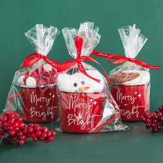 three red mugs with frosting and marshmallows wrapped in cellophane