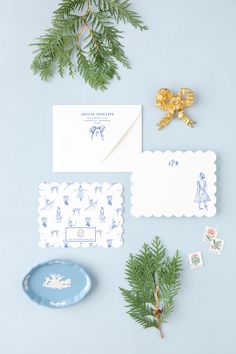 the stationery is laid out on top of the blue surface with pine branches and place cards