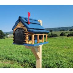 a small wooden house with a blue roof in the middle of a grassy field next to a mailbox