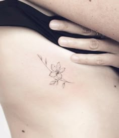 a woman's stomach with a small flower tattoo on her left side ribcage