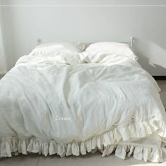 an unmade bed with white linens and ruffled bedspread on the floor