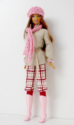 a barbie doll wearing winter clothes and pink boots with a scarf on her head, standing in front of a white wall