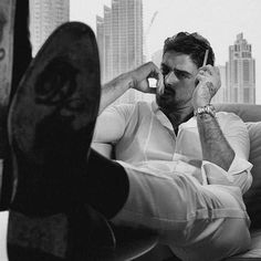 a black and white photo of a man sitting on a couch talking on his cell phone