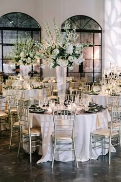 the tables are set with white linens and centerpieces in tall vases