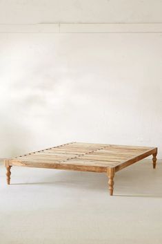 a wooden bed frame sitting on top of a white floor next to an empty wall