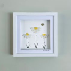 three daisies in a white frame with a bee