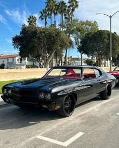 two classic muscle cars parked next to each other in a parking lot with palm trees