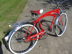 a red bicycle parked on the side of a road next to a tree and grass