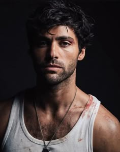 a man in white tank top and necklace with blood on his face looking at the camera