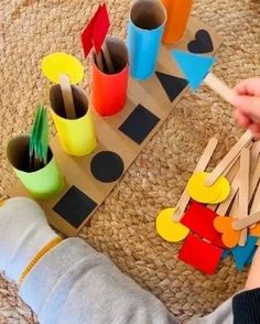 a child is playing with wooden pegs and construction paper cups on the floor in front of them