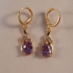 These Beautiful Purple Topaz Ribbon Swirl Earrings Are Made Of 18k Yellow Gold Filled. The Large Oval Topaz Zircon (Lab Created) Stones Are 6x8mm And With A Swirl Of Smaller White Topaz Stones. Brand New And Never Been Worn. Lead And Nickel Free. These Fine Quality Earrings Are Perfect And Comfortable For Special Occasions Or A Special Gift. Please Send Offers And Questions. Big Stone :6 X 8mm Or .24" X .31" Earrings: 1.22" X .31" Fastening: Hoop Clasp (Pierced) Hoop Diameter: .47" Elegant Gold Amethyst Crystal Earrings, Amethyst Earrings Gold, Purple Amethyst Earrings, Purple Gems, Swirl Earrings, Amethyst Jewelry, Topaz Stone, Amethyst Earrings, White Topaz