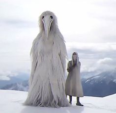 a large bird standing next to a woman on top of a snow covered slope